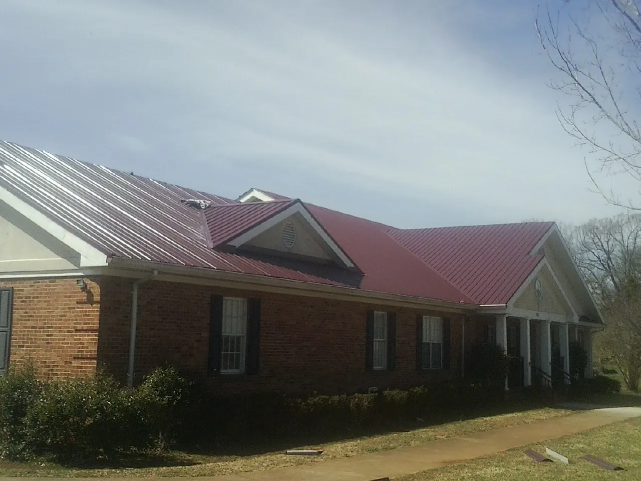 Red metal roof with gabled entries on a long brick building, from a Hail Damage Roof Repair job in Columbia